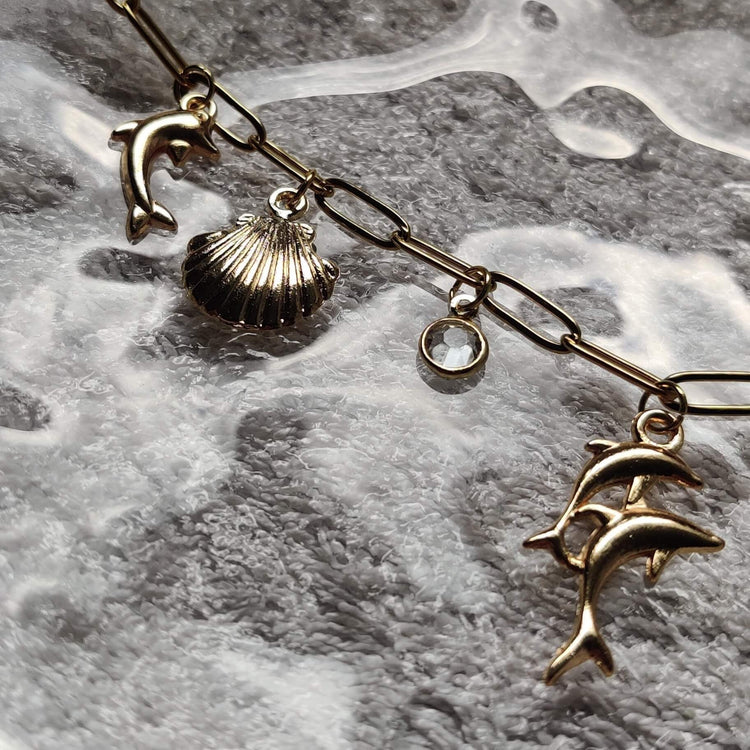 Zoom sur les charms du collier doré Danse Océane – coquillage, dauphin – Roxy Paris